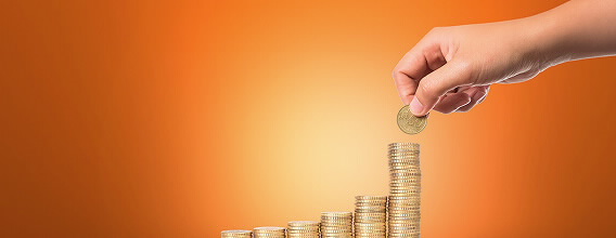 DP BPI Novos Montantes. Uma mão a colocar uma moeda numa pilha de moedas maior que as restantes.