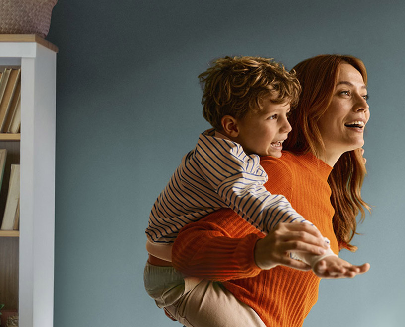 BPI Reforma Vida PPR. Imagem de uma mãe sorridente, em casa, com uma criança sorridente às cavalitas.